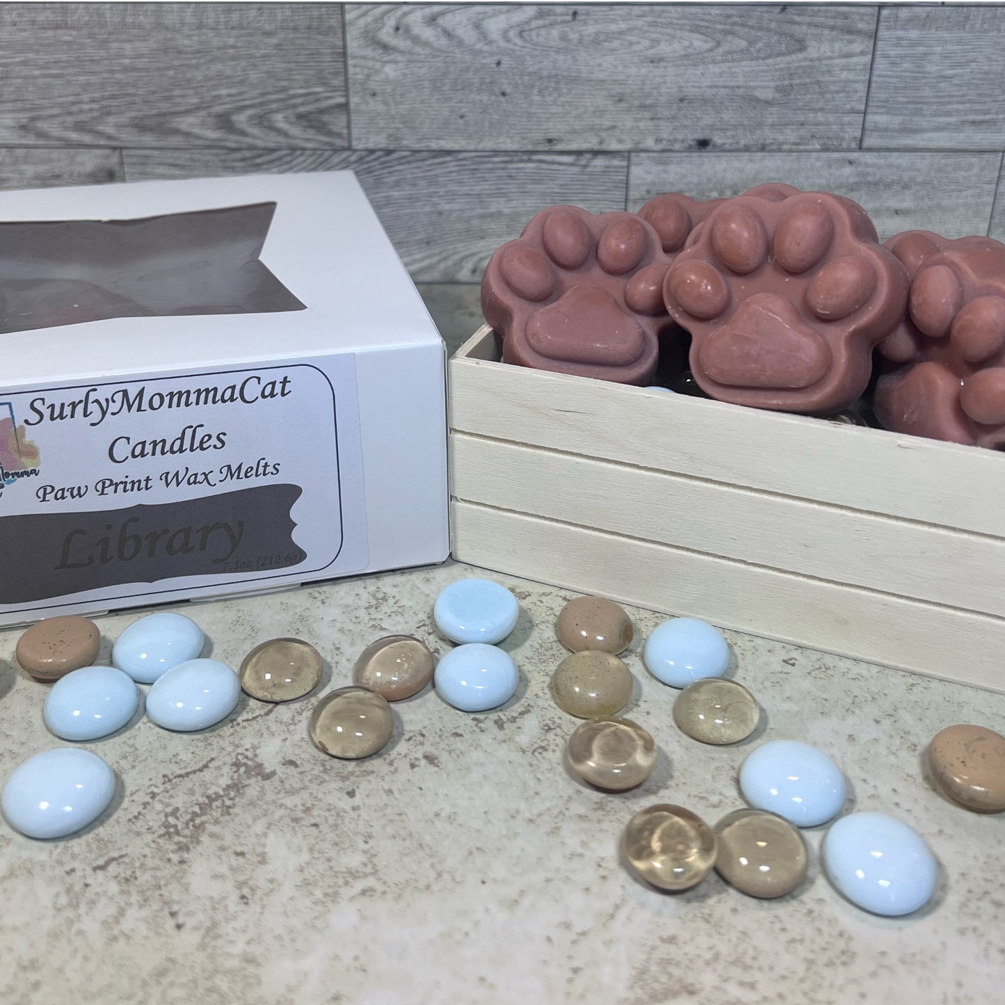 Brown Library soy wax melt paw prints in a wooden box with decorative rocks and white box product packaging for the Library paw prints.
