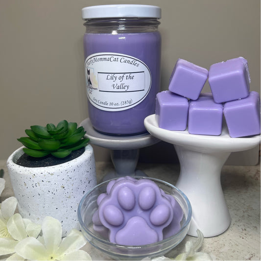 Light Purple Lily of the Valley Soy Glass Jar candle, with cube and paw print wax melts on small white pedestals, with a small plant for decor.