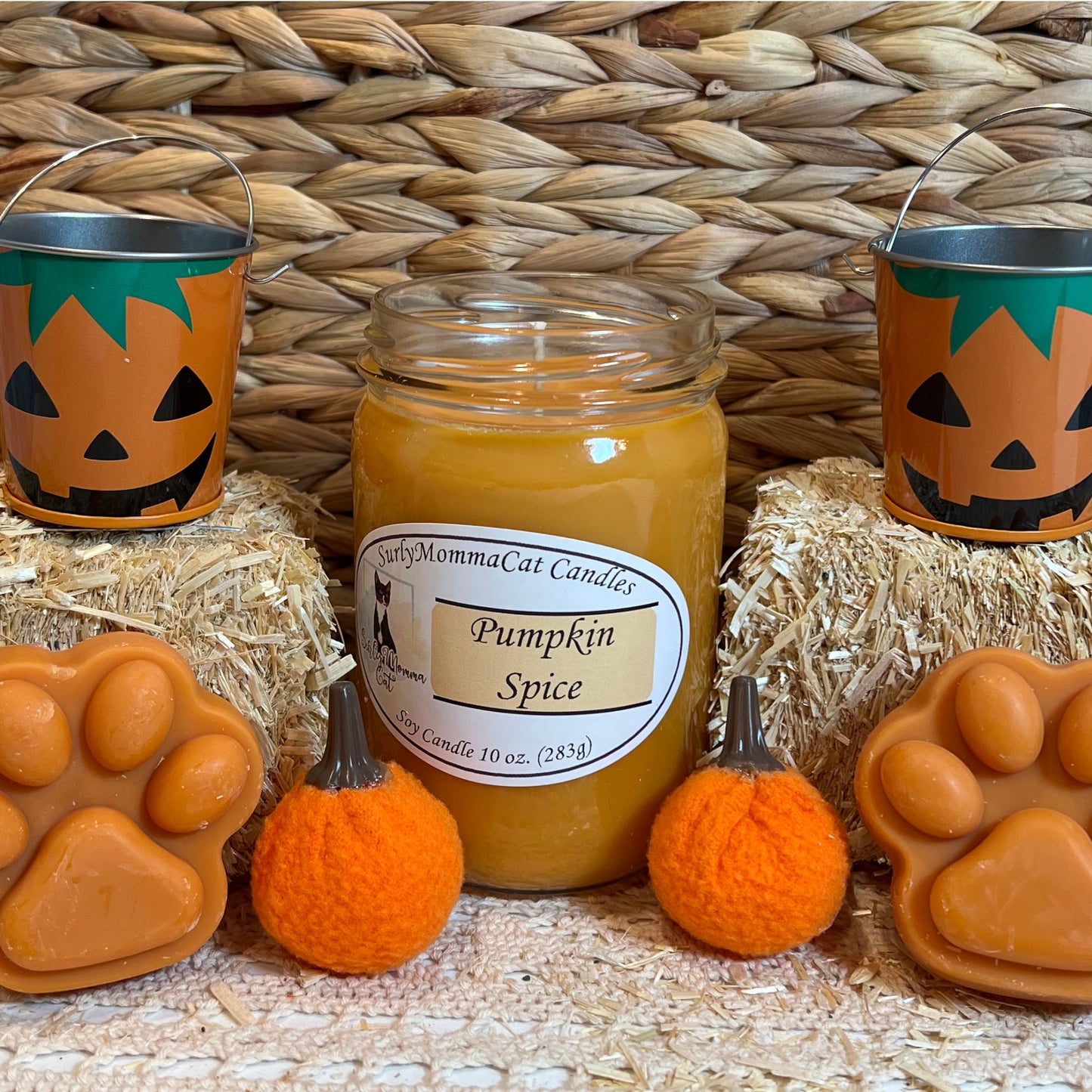 Orange Pumpkin Spice soy glass jar candle, with wax paw prints. two small pumpkin pails sitting on tiny decorative hay bales.