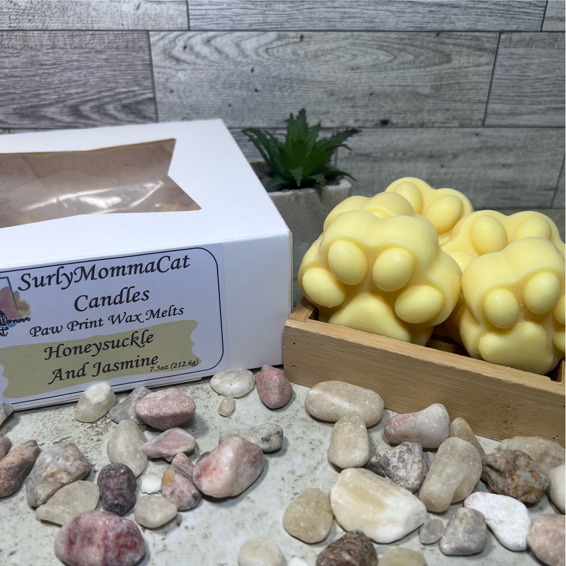 Yellow Honeysuckle and Jasmine soy wax melt paw prints, in rustic box, with white box labeled Honeysuckle and Jasmine, with decorative rocks and plants.