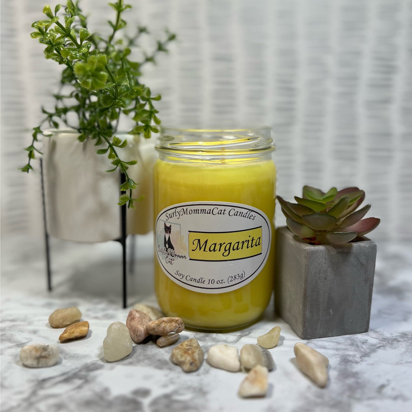Yellow soy Margarita candle with decorative rocks and small plants for decor.