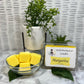 Bowl of cubed yellow margarita wax melts with clam shell wax container and green leaves and plants for decor.