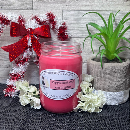 A warm scented Peppermint and Eucalyptus Christmas scene, with the featured candle in the front, littered with lovely white flowers,  a green plant, and a red and white Christmas candy cane wreath as background decoration.