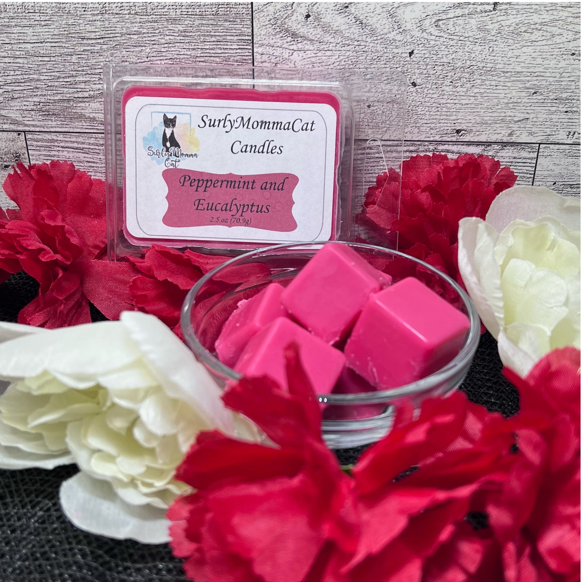 A warm scented Peppermint and Eucalyptus Christmas scene, with the featured wax melts in both it's packaging box and in a bowl ready for use, accenting the scene as background decoration lies red and white flowers,  creating a lovely foundation of holiday cheer.