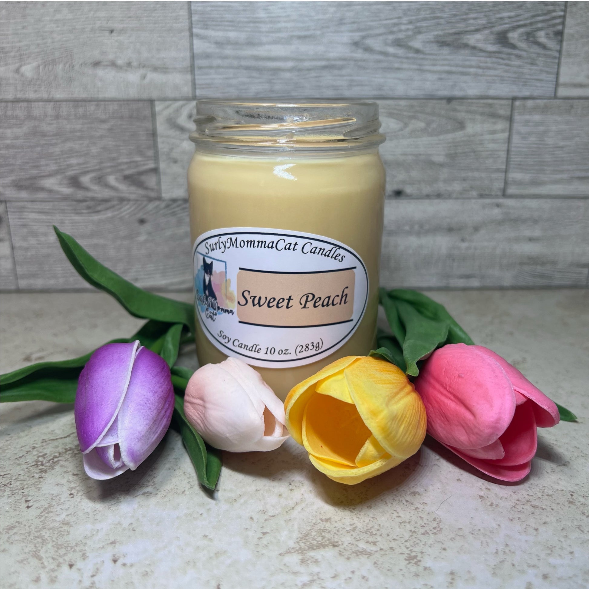 Tan Sweet Peach soy glass jar candle with some pink, purple, tan, yellow flowers for decoration.